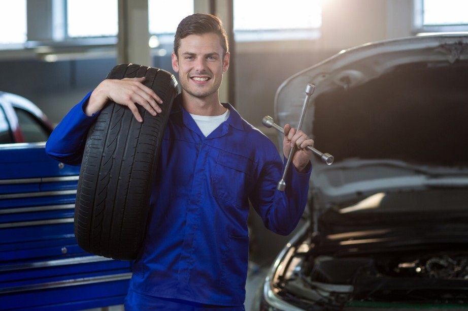 Mecánico sonriente sosteniendo un neumático y una llave de ruedas en un taller automotriz profesional
