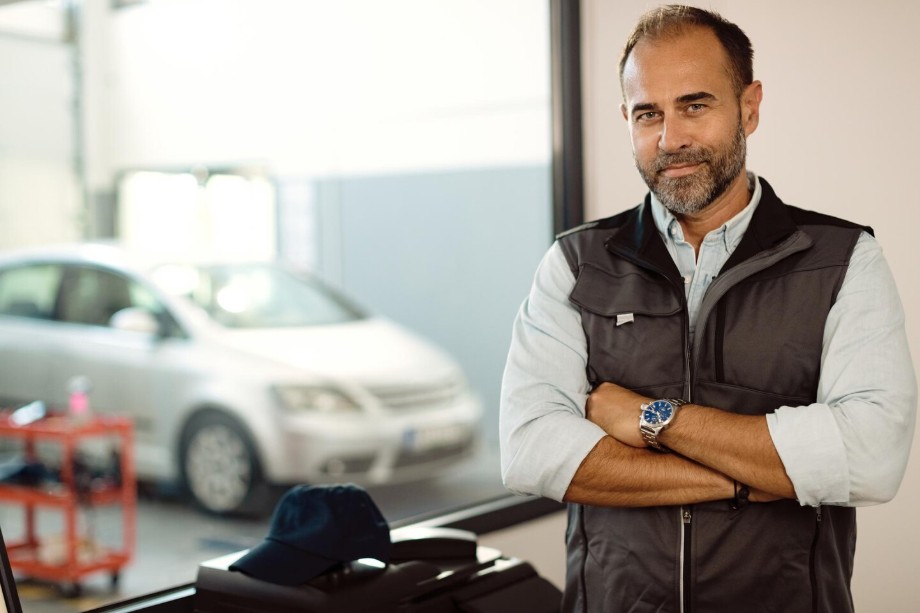 Asesor de servicio automotriz en el mostrador con un vehículo visible en el taller