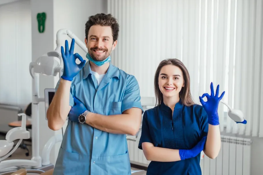 Profesionales dentales con uniformes médicos haciendo señal de OK en un consultorio dental moderno