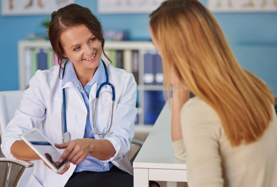 Médica mostrando información de tratamiento en una tablet a una paciente en un consultorio